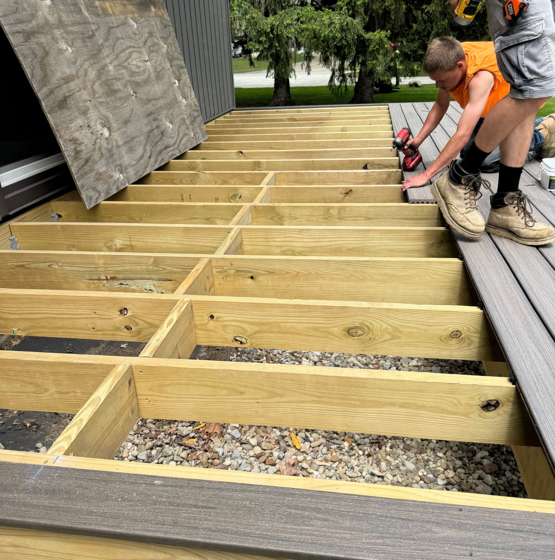 Person installing composite deck boards on a wooden frame. Outdoor setting.