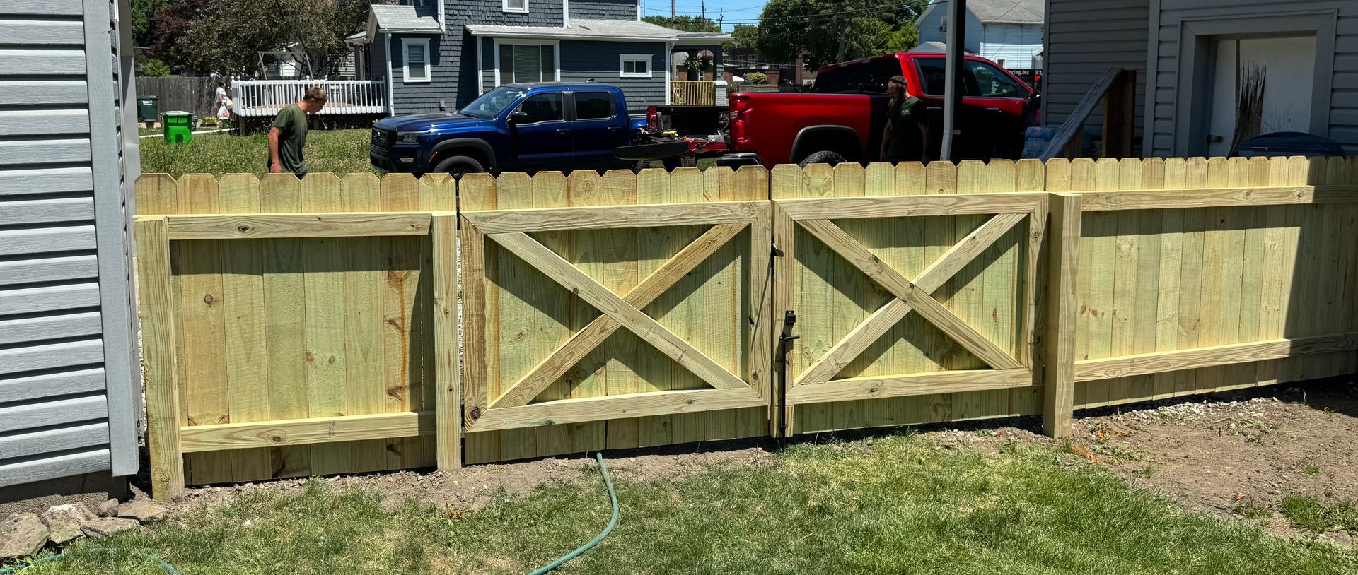 Wooden fence with gate and vehicles in the background.