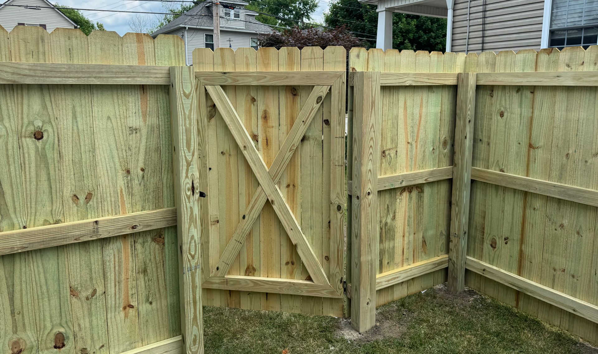 Wooden fence with gate in yard. Greenish planks, X-braced gate, horizontal rails.