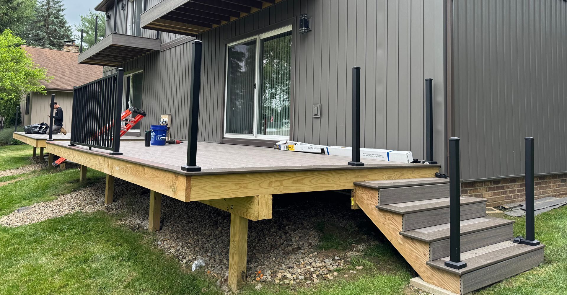 Deck with black railings and steps, attached to a gray house with a sliding glass door.