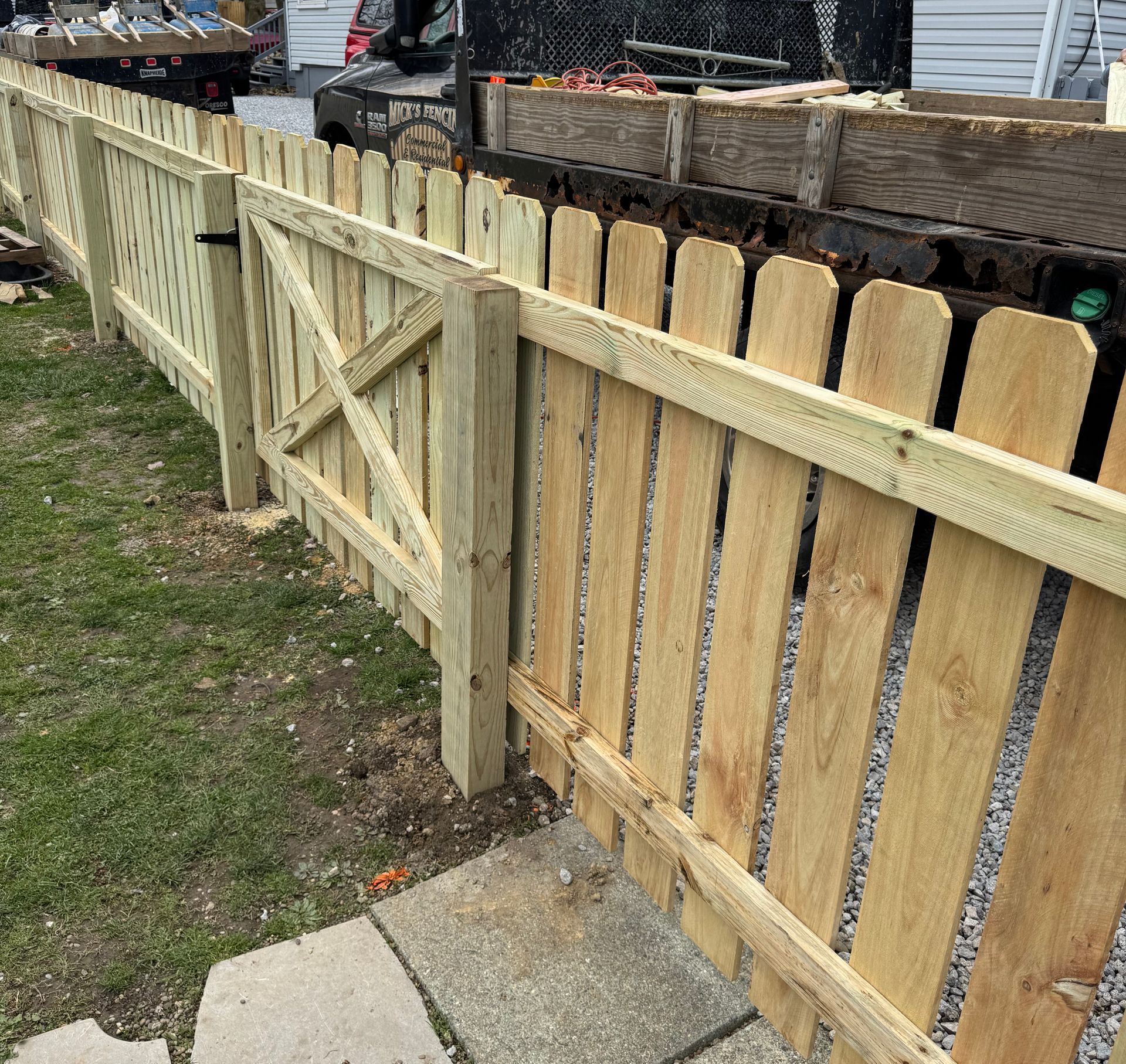 Wooden fence with gate, newly constructed, in front of grass and gravel, daylight.