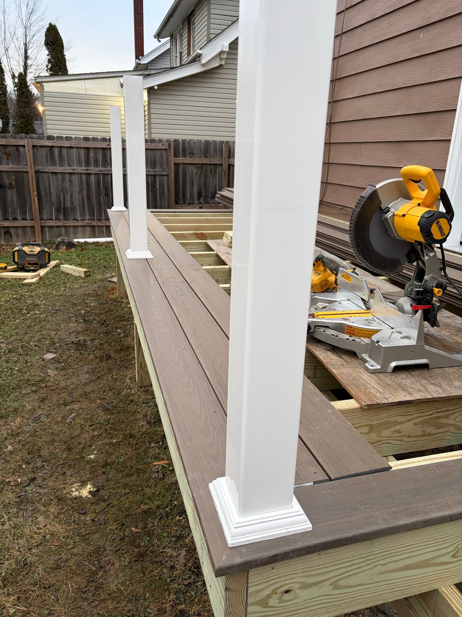 Deck with white posts under construction; a miter saw sits nearby