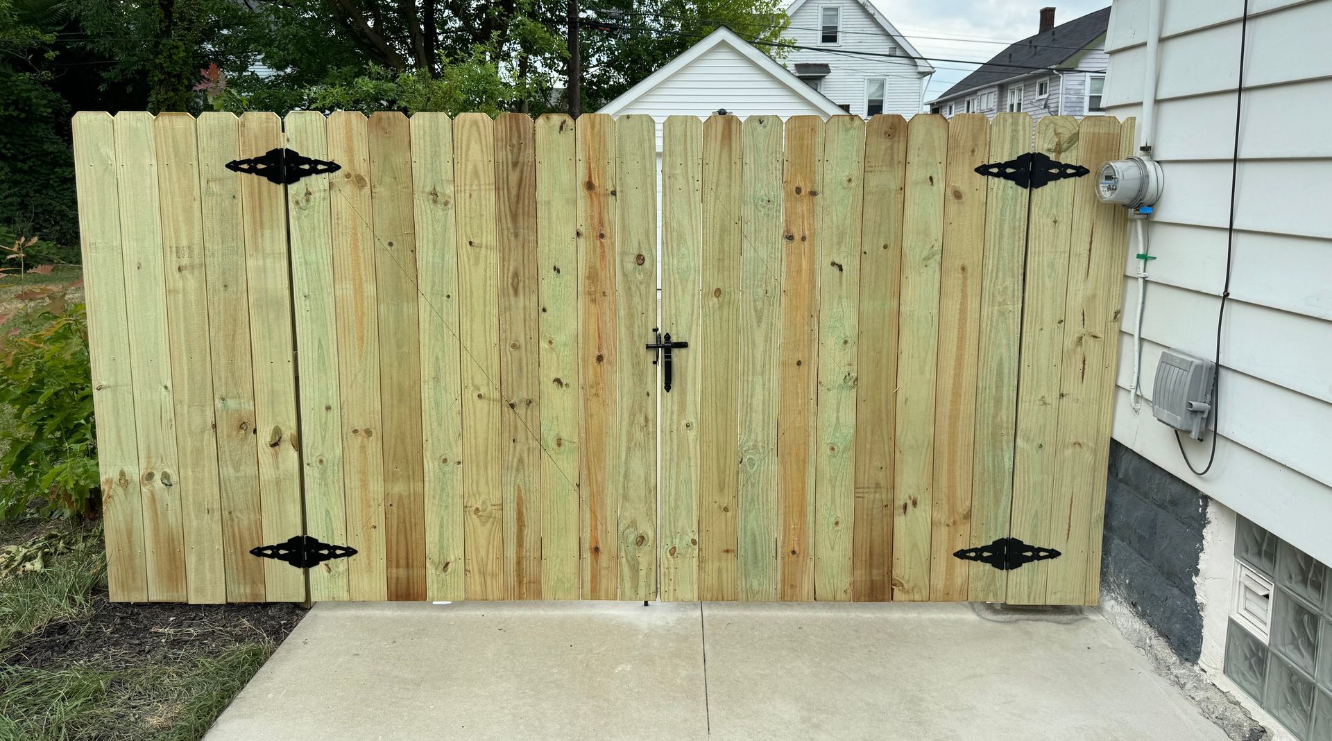 Wooden double gate with black hardware against a light-colored house and concrete.