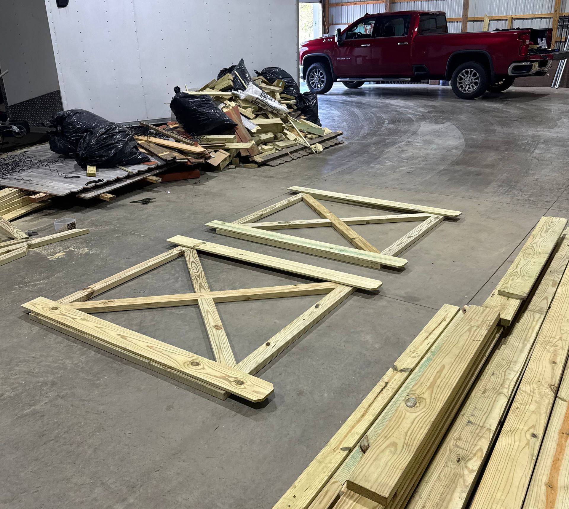 Two wooden frames, with an X brace, next to wood scraps, and a red truck in a warehouse.