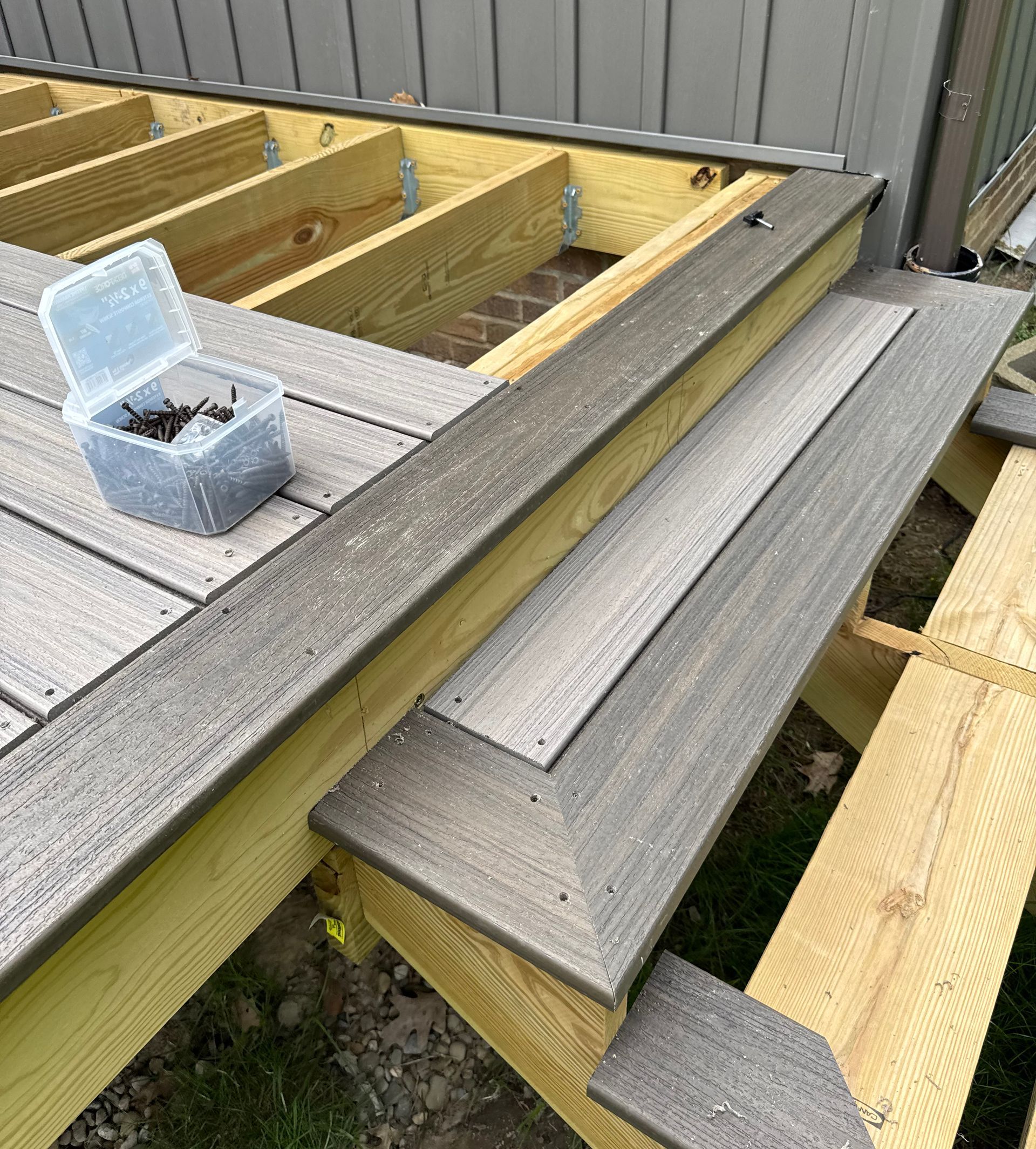 Deck construction: composite boards being installed on a wooden frame. Gray and brown tones.
