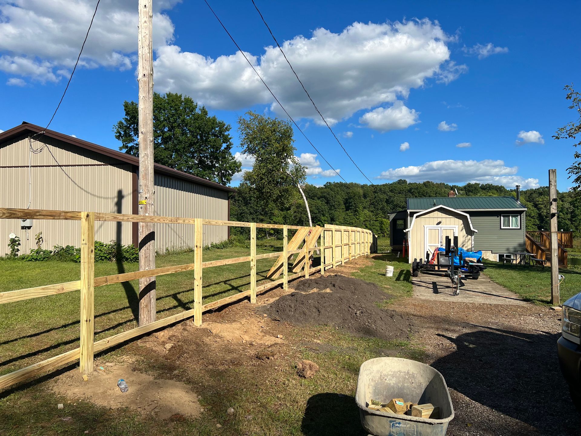 New wooden fence being built next to a grassy yard, with a shed and house visible on a sunny day.