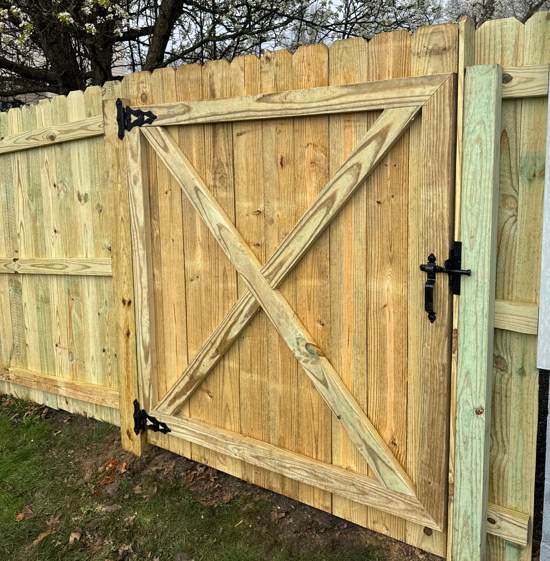 Wooden gate in a wooden fence, featuring an X-shaped brace.