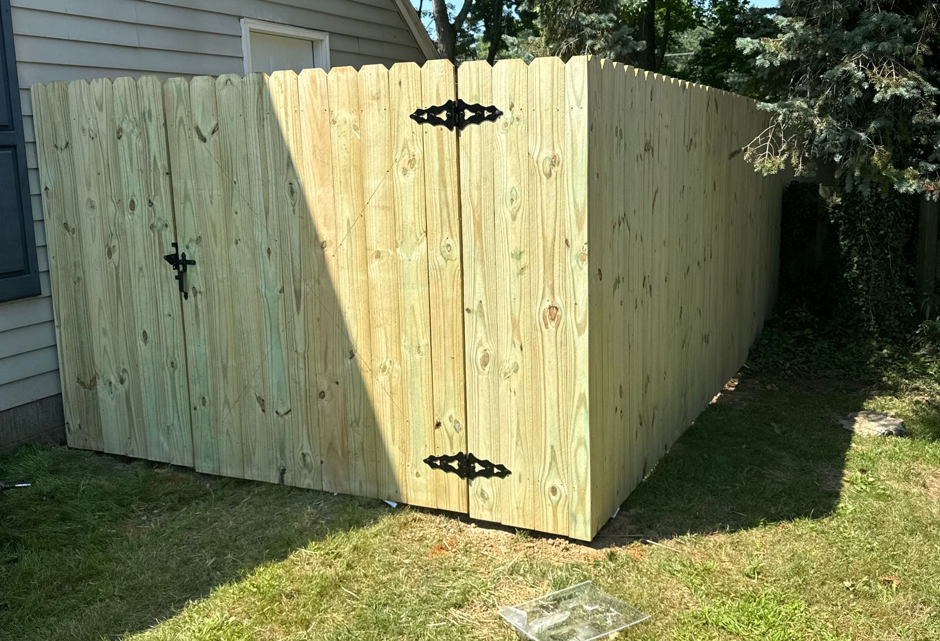Wooden fence with two closed doors and black hinges.