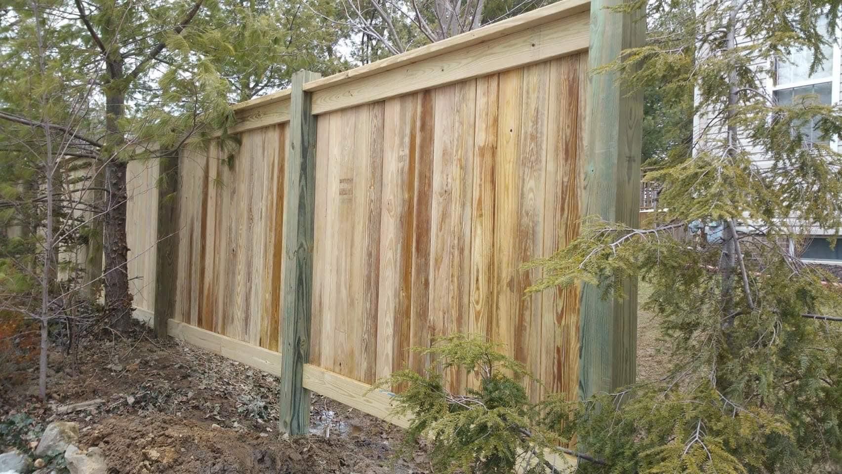 Wooden privacy fence with weathered boards, surrounded by trees and bushes.