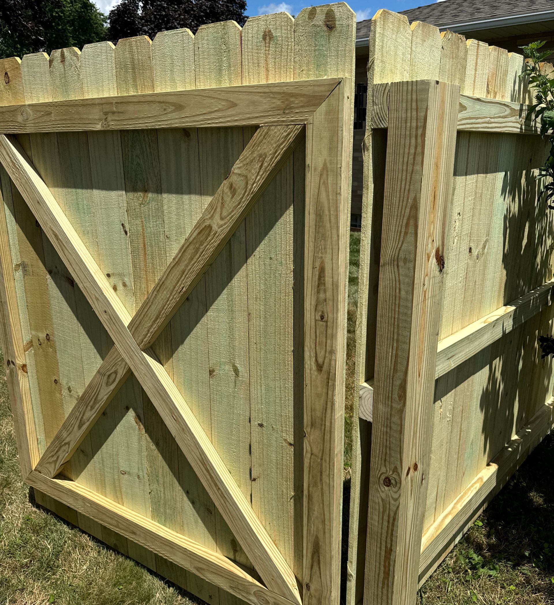 Wooden gate with an X-shaped brace, set in a wooden fence.