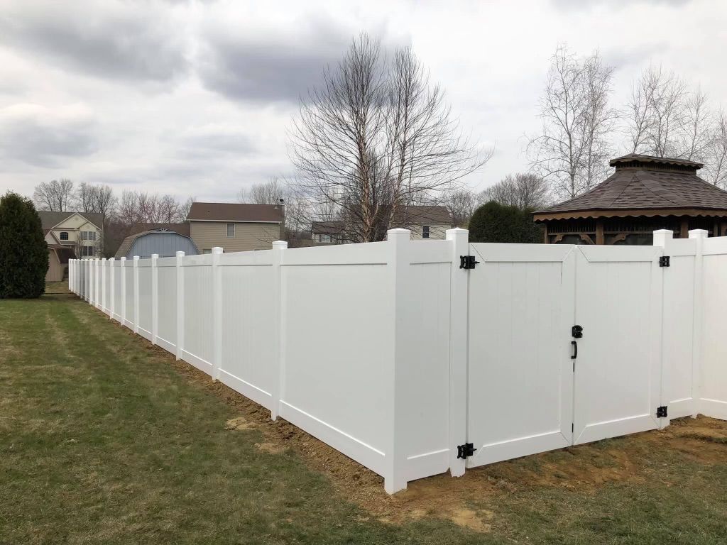 White vinyl fence enclosing a grassy backyard on an overcast day, with a gate and small gazebo visible.