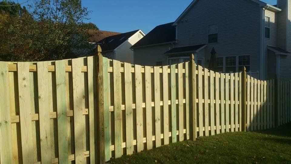 Wooden fence in a backyard, with a house in the background under a blue sky.