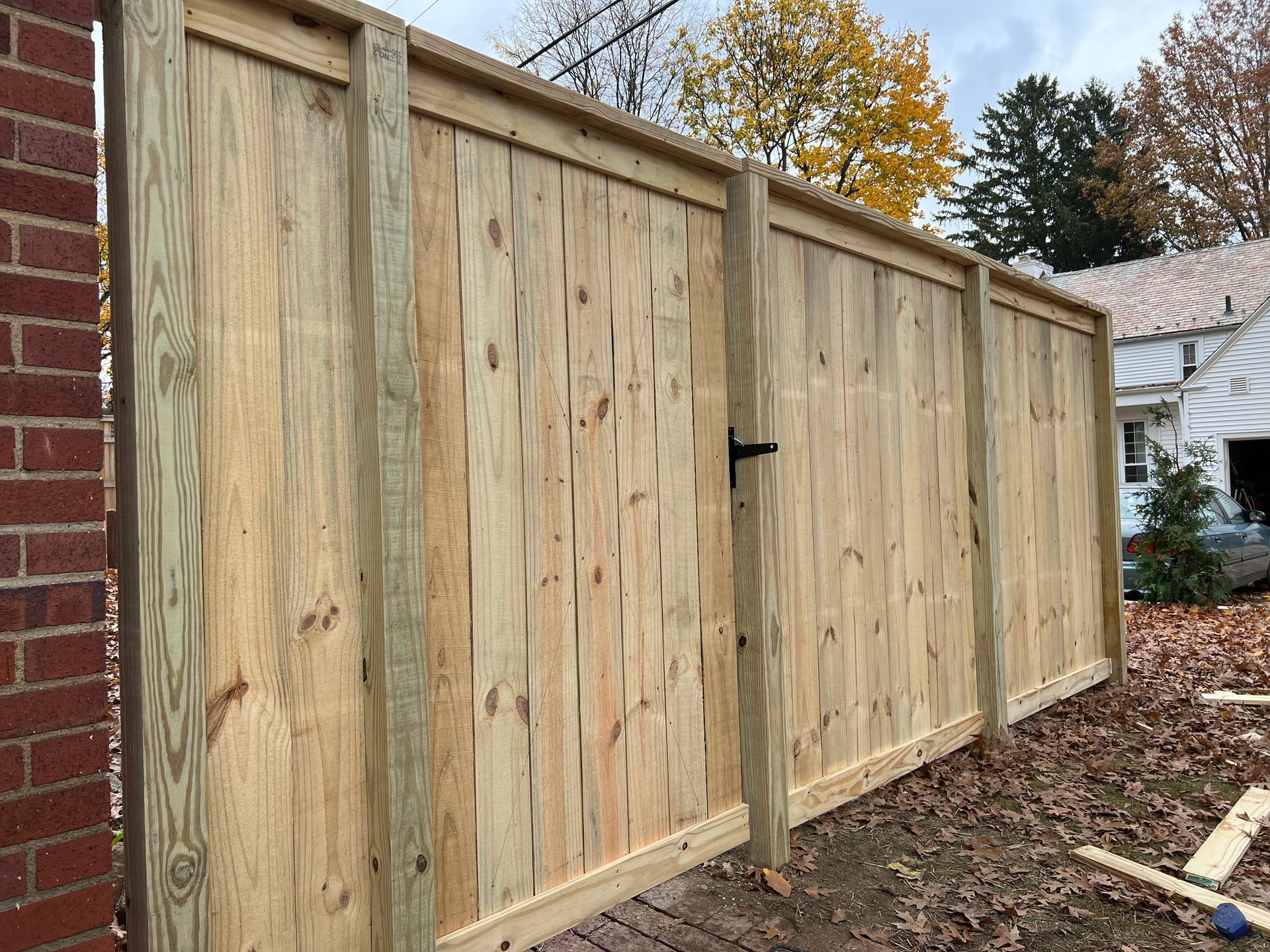 Wooden privacy fence with a gate next to a brick wall and a house in the background.