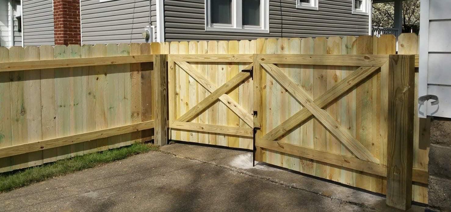 Wooden gate and fence, X-braced gates, light wood, concrete surface, grass.