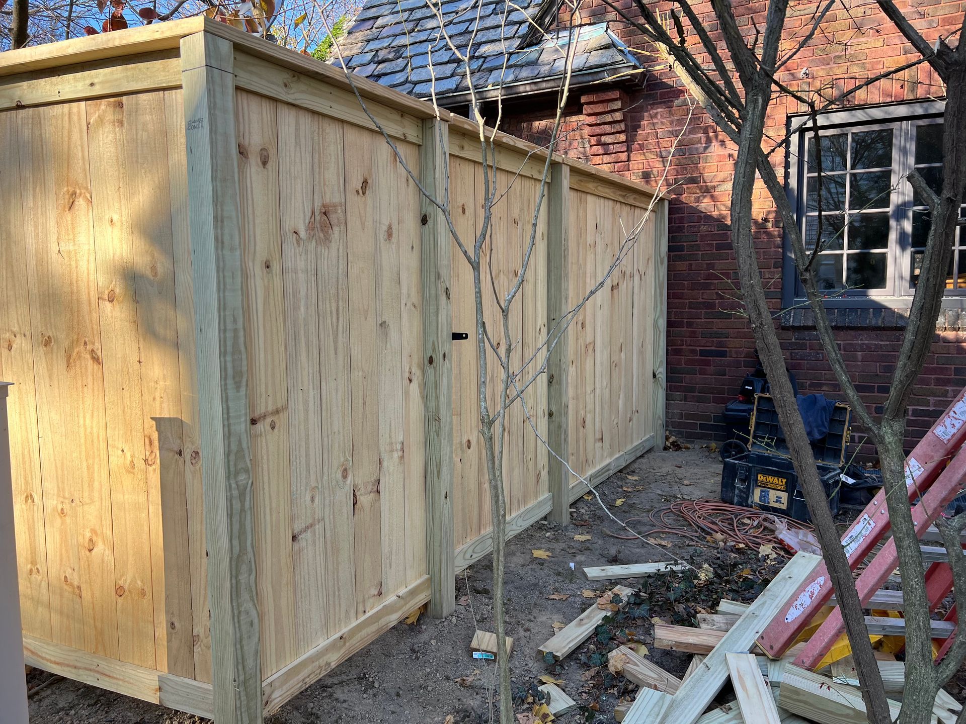 Wooden fence in a yard next to a brick building with a window.