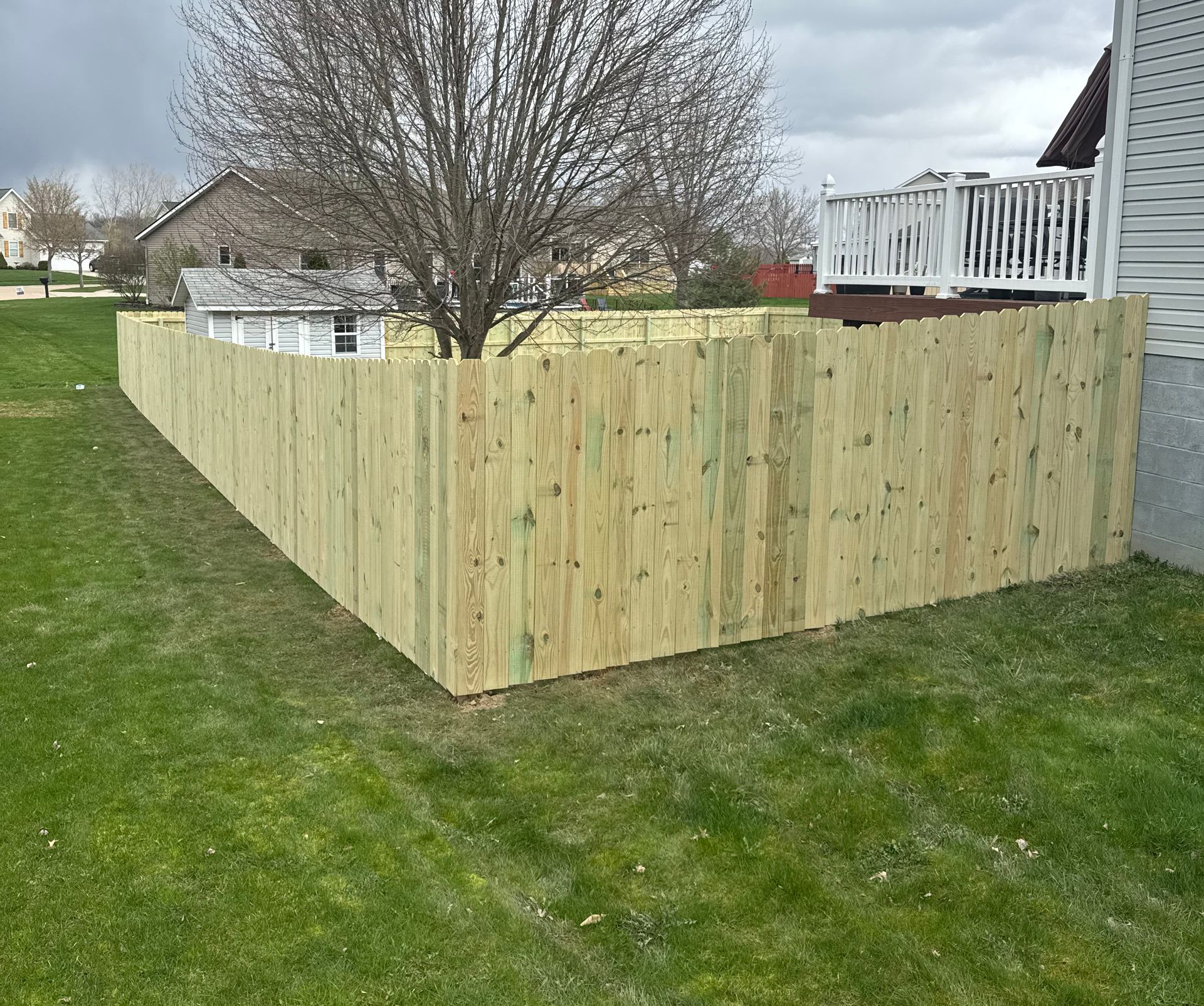 Wooden fence in a grassy yard, extending along a property line, houses in background.