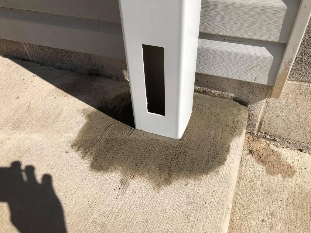 White downspout draining water onto a concrete surface next to the side of a light-colored house.