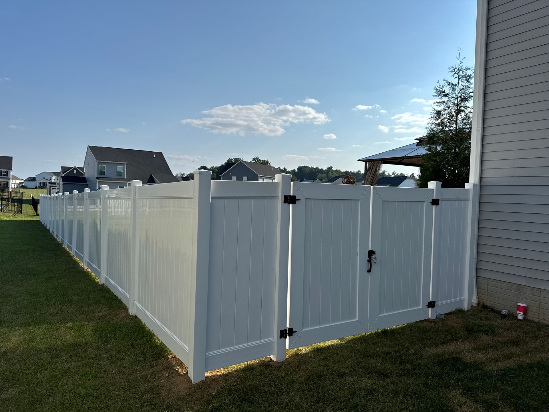 White vinyl fence with a gate on a grassy lawn against a bright blue sky.