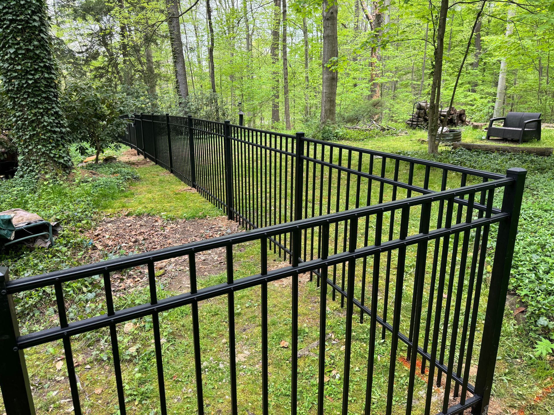 Black metal fence enclosing a grassy yard with trees in the background.
