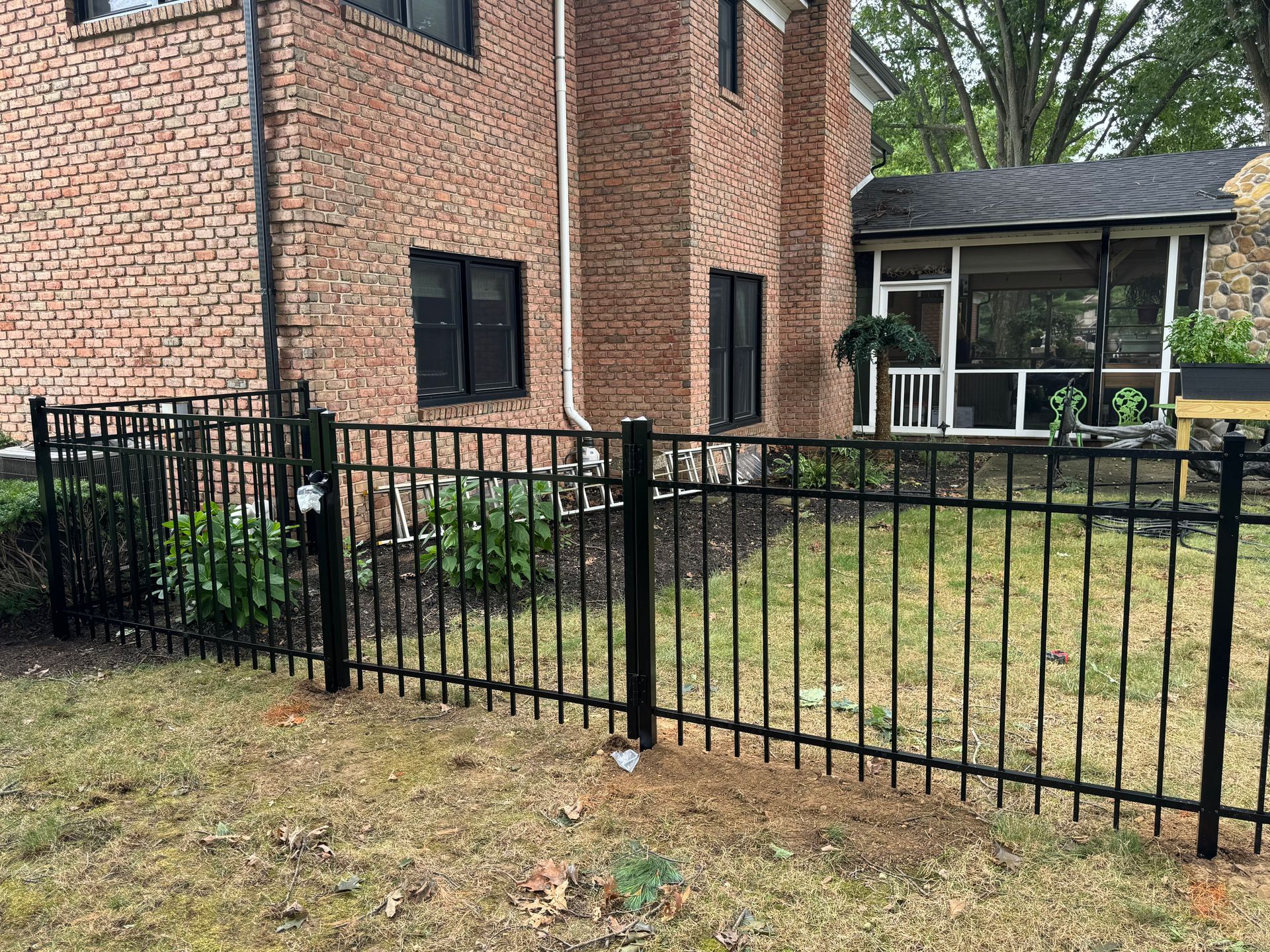 Black metal fence in front of a brick house with a screened porch and green lawn.