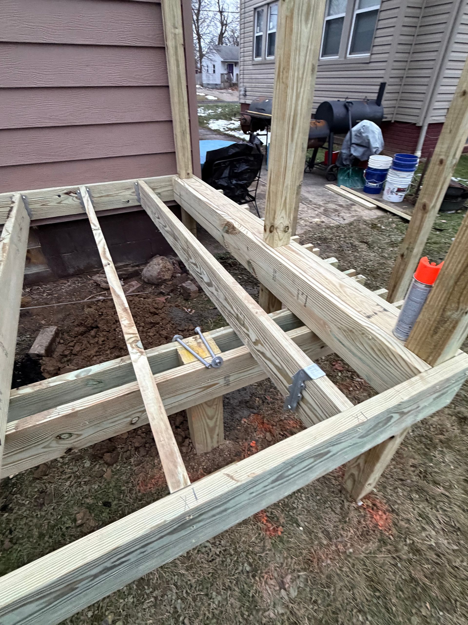 Wooden deck under construction next to a house with exposed framing and beams
