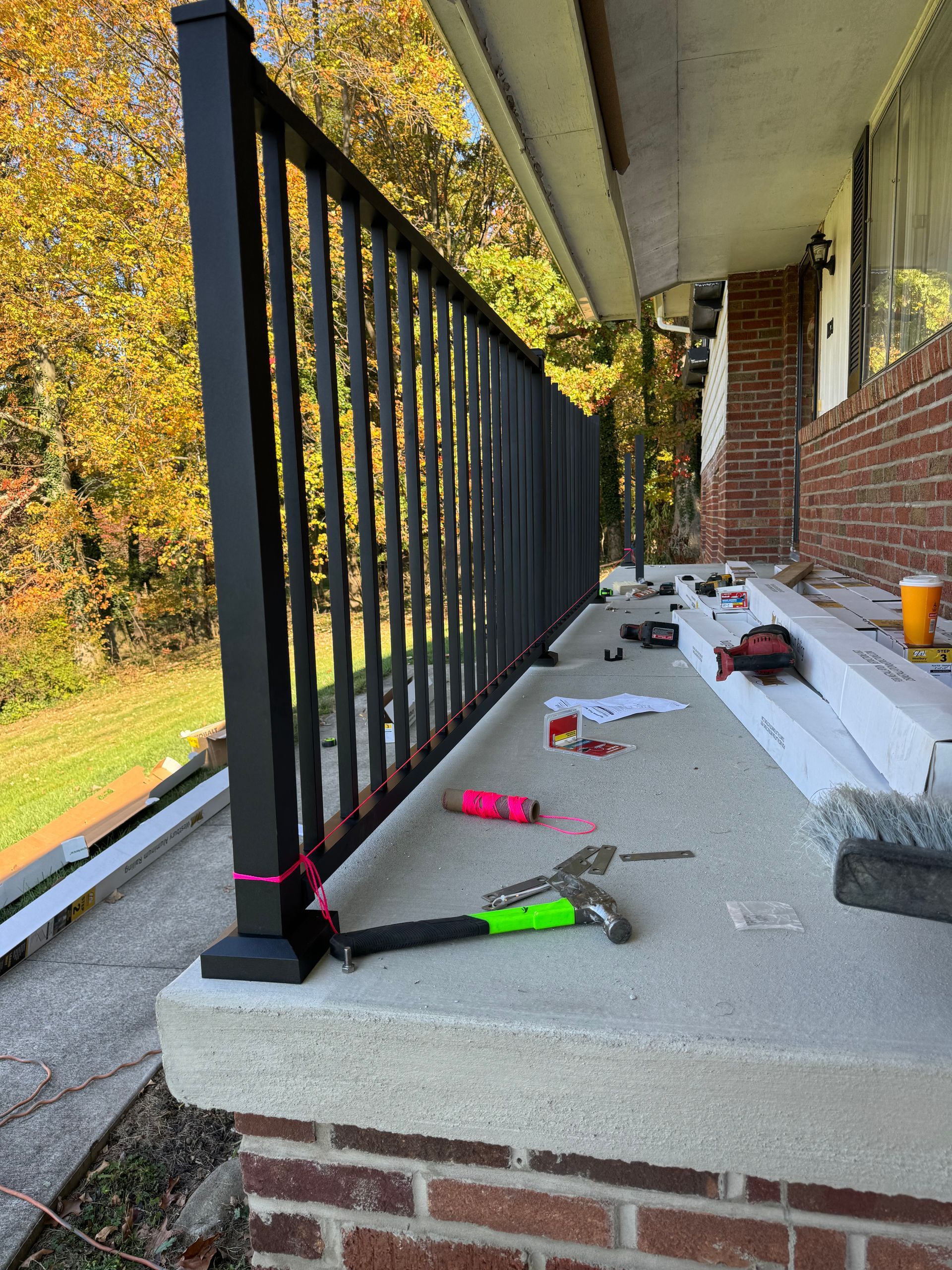 Black railing installed on a porch with tools and materials scattered, in front of a brick home.