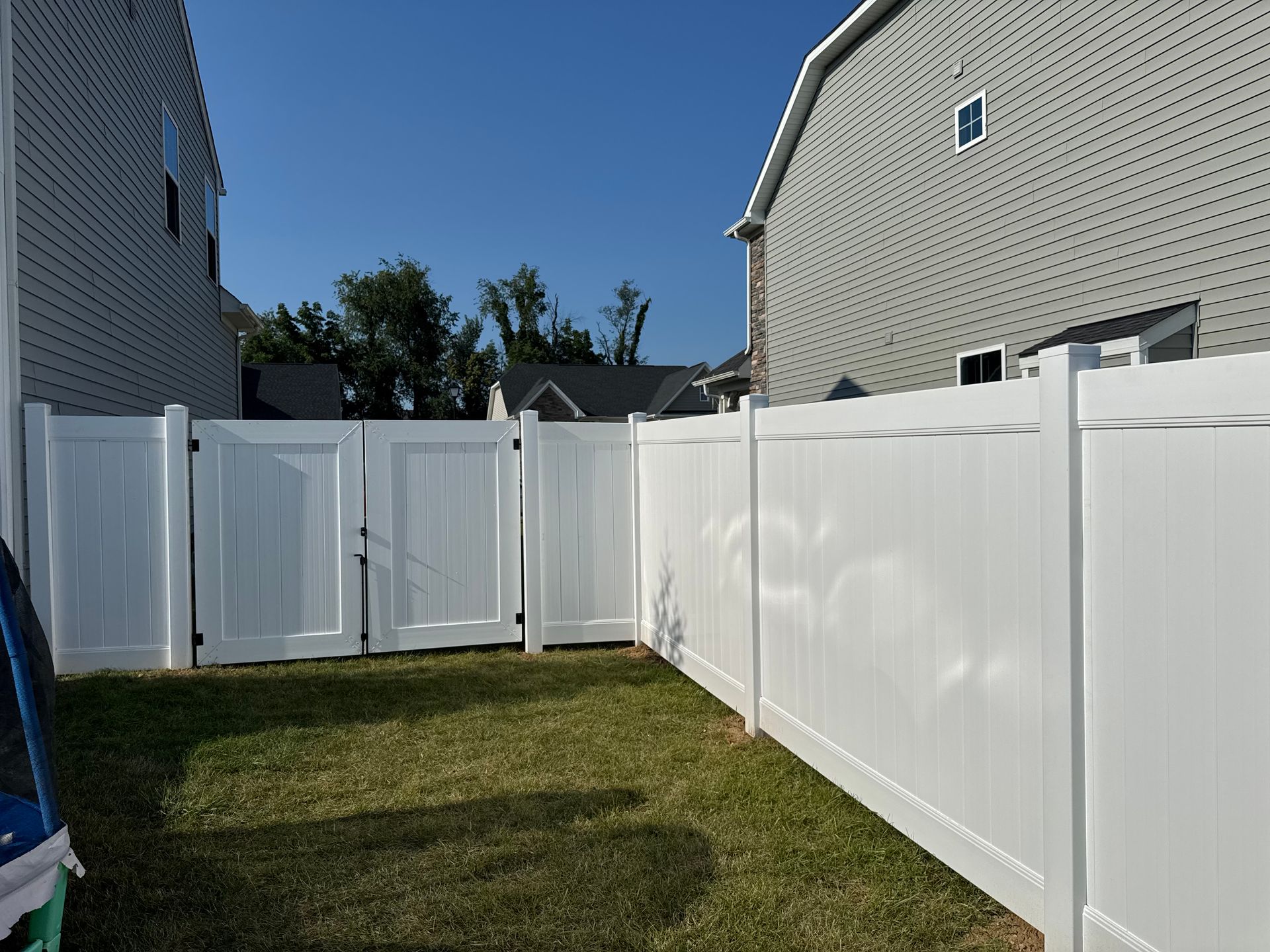 White vinyl fence with a gate in a backyard between two houses.