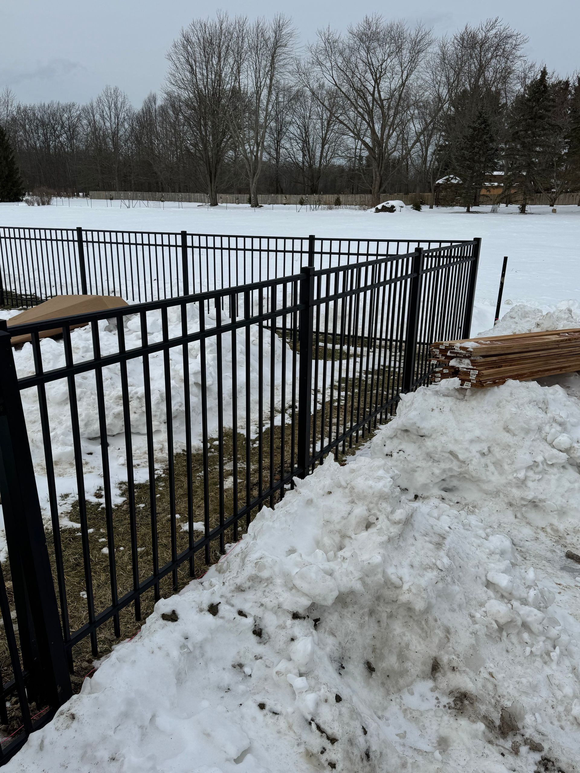 Black metal fence with snow piled along it, snowy field in the background.