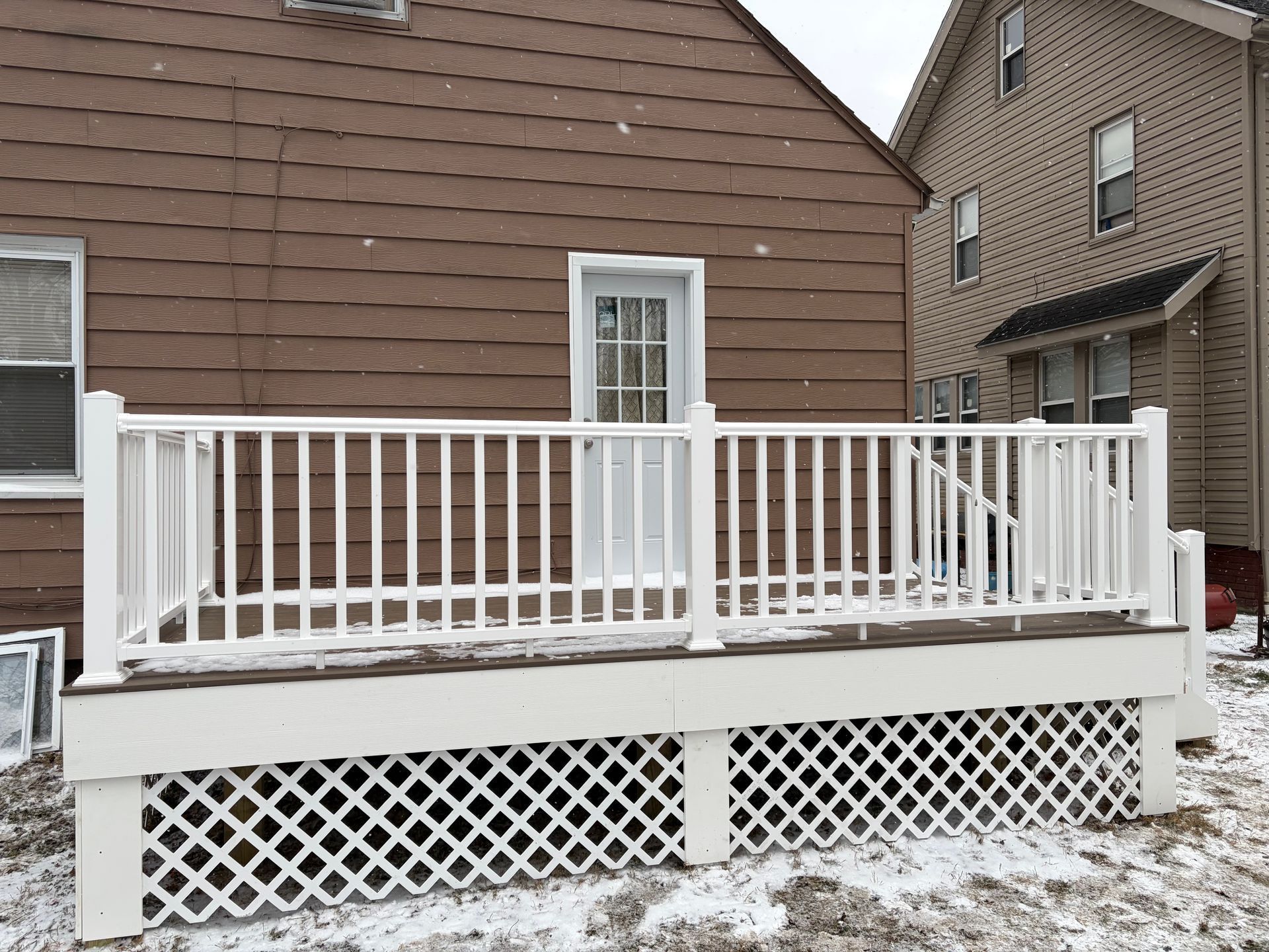 White deck with lattice skirting and railing, leading to a door on a brown house