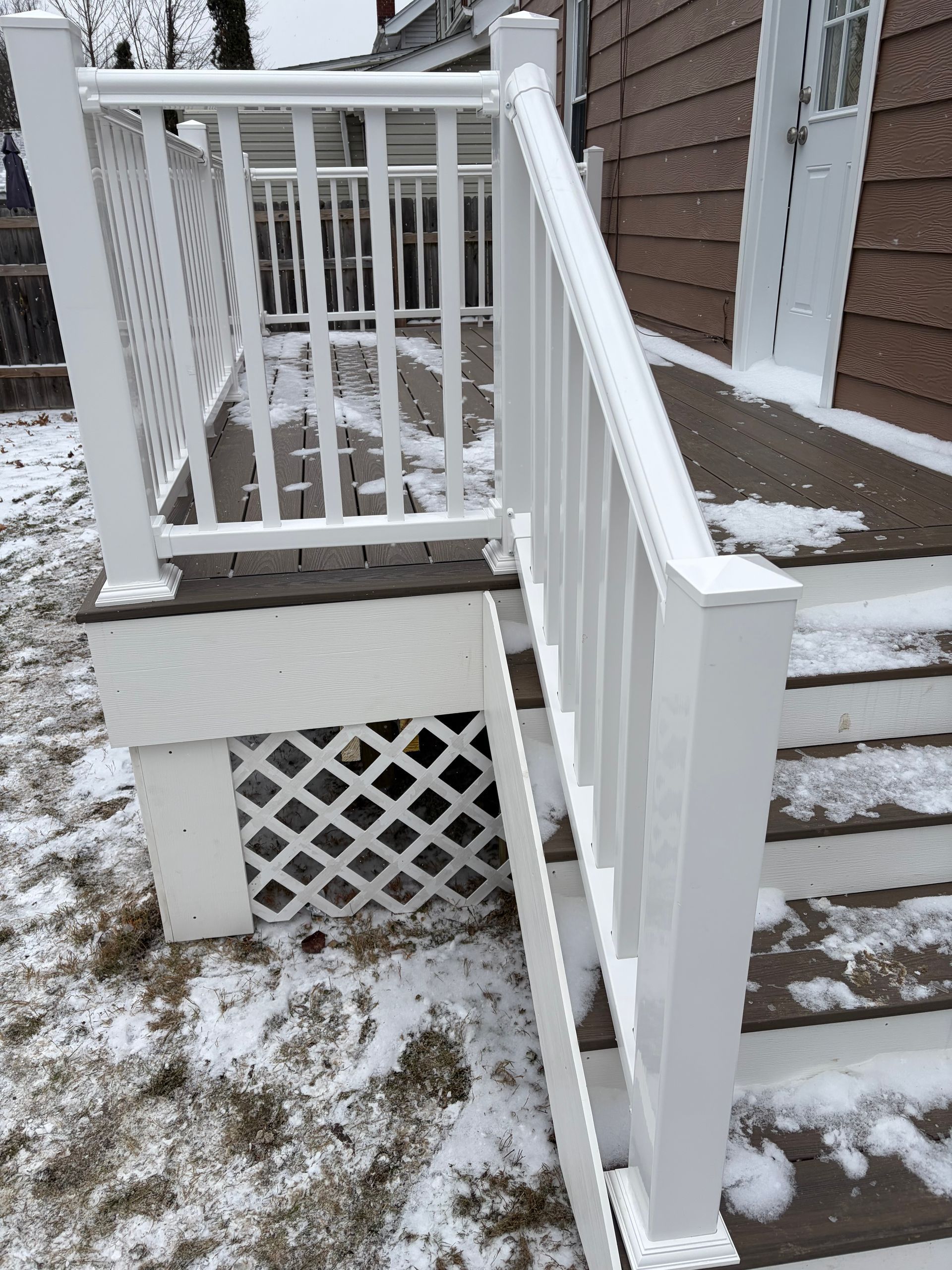White deck and stairs with latticework and railing, set in a snowy yard