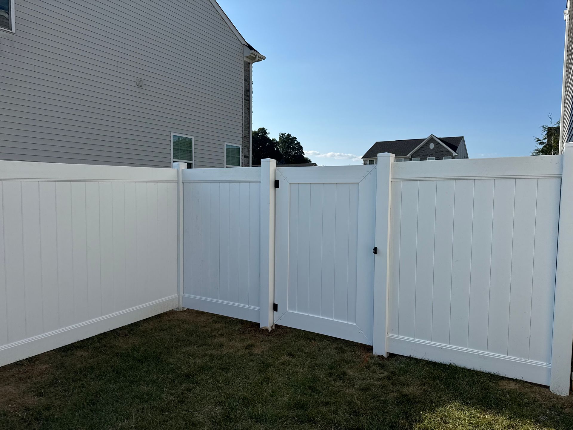 White vinyl fence with a gate in front of a house on a sunny day.