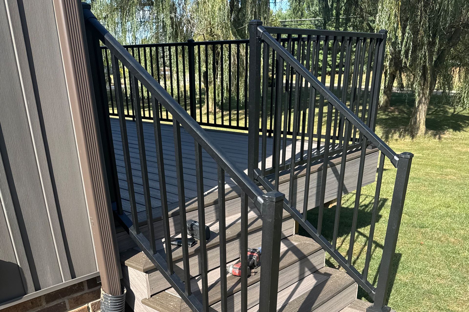 Black deck with stairs, railing, and a green lawn in the background.