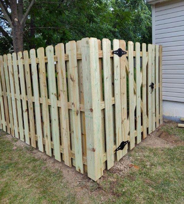 Wooden fence with cross-braced panel and chain link, in a grassy yard next to a brick building.