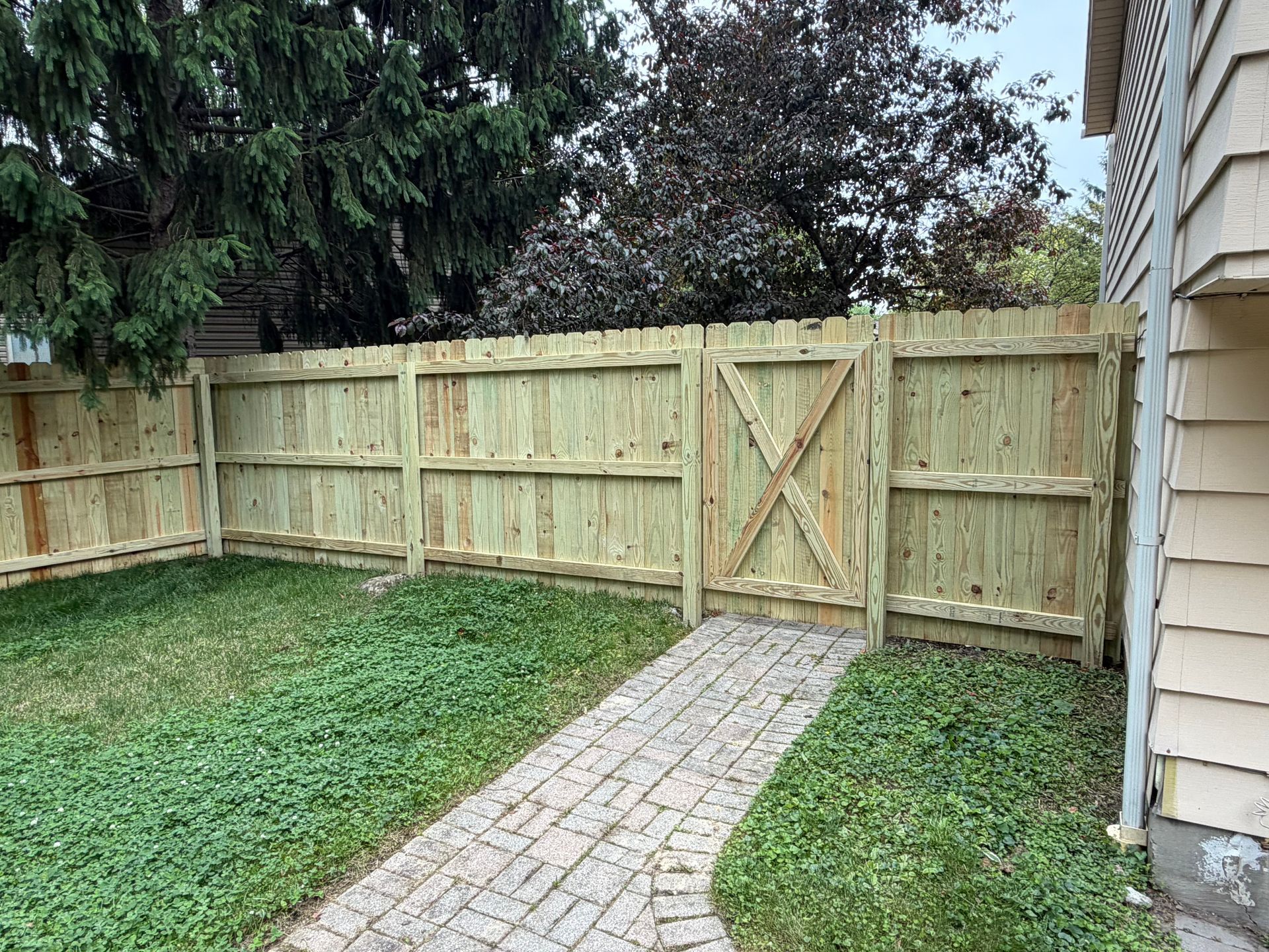 Wooden backyard fence with a central gate beside a stone walkway and lawn