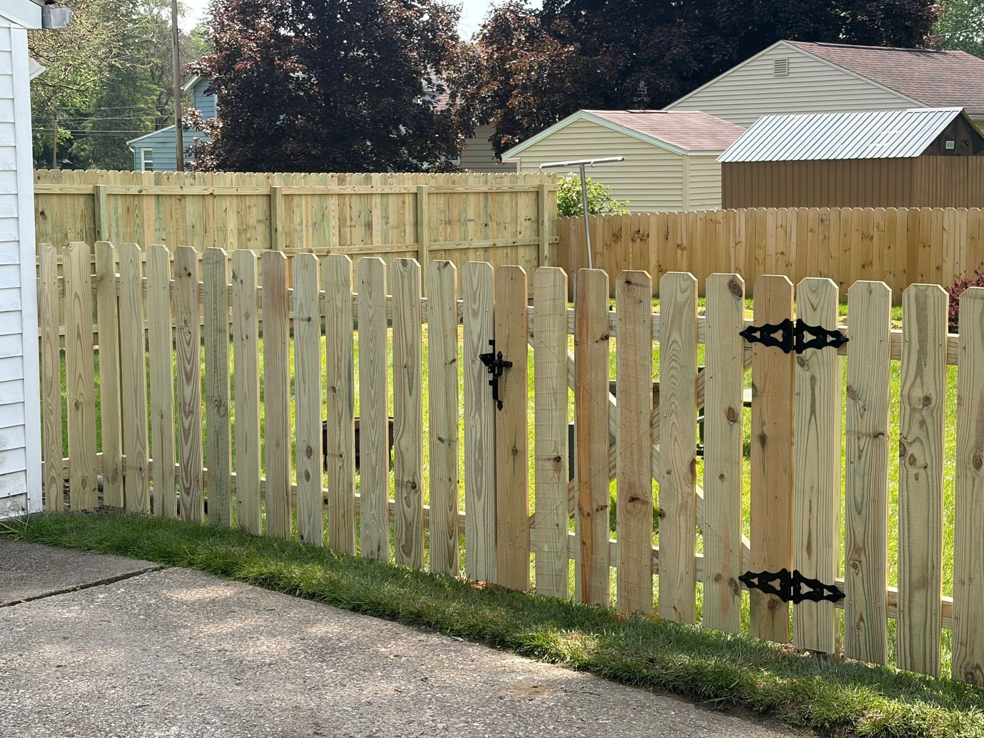 Wooden backyard fence with black hinges and a gate, beside a gravel path and lawn.