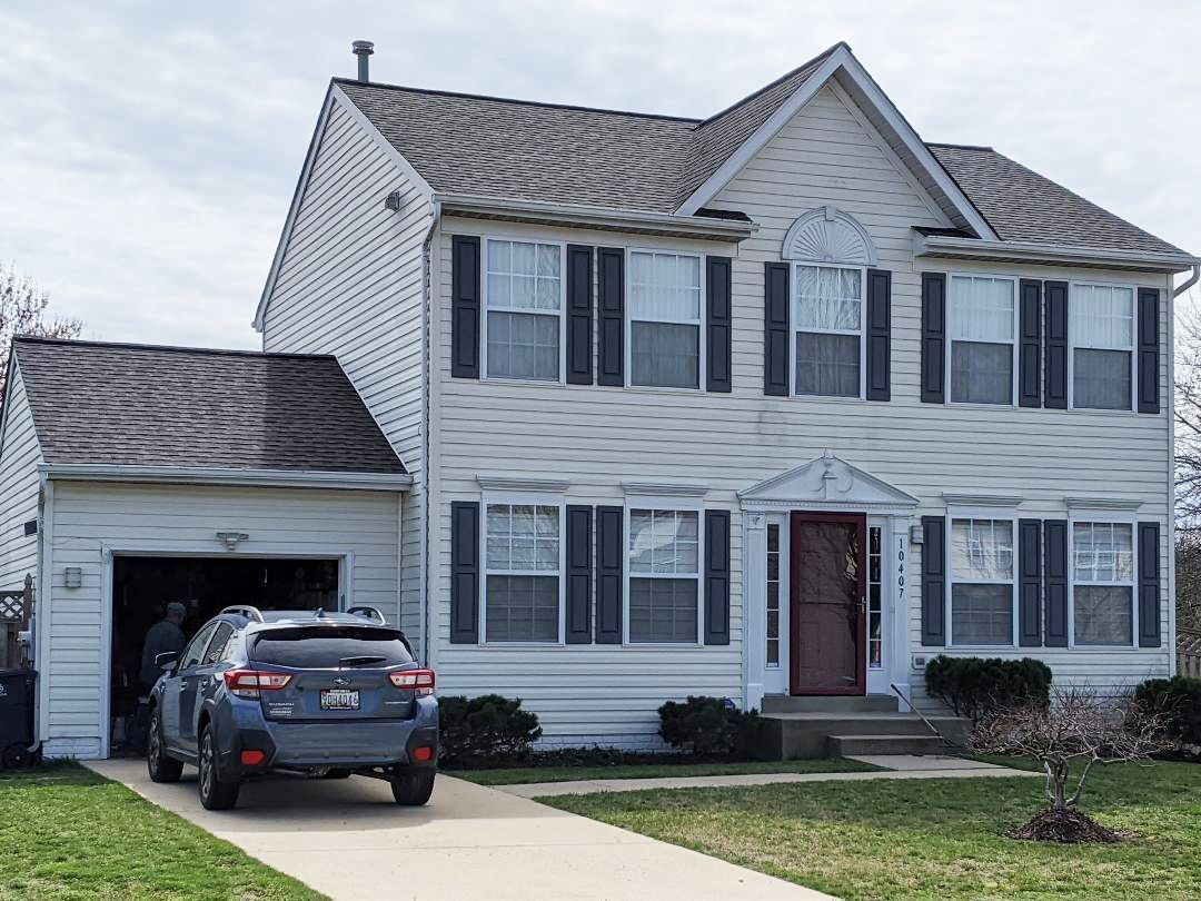 a car is parked in front of a white house with black shutters