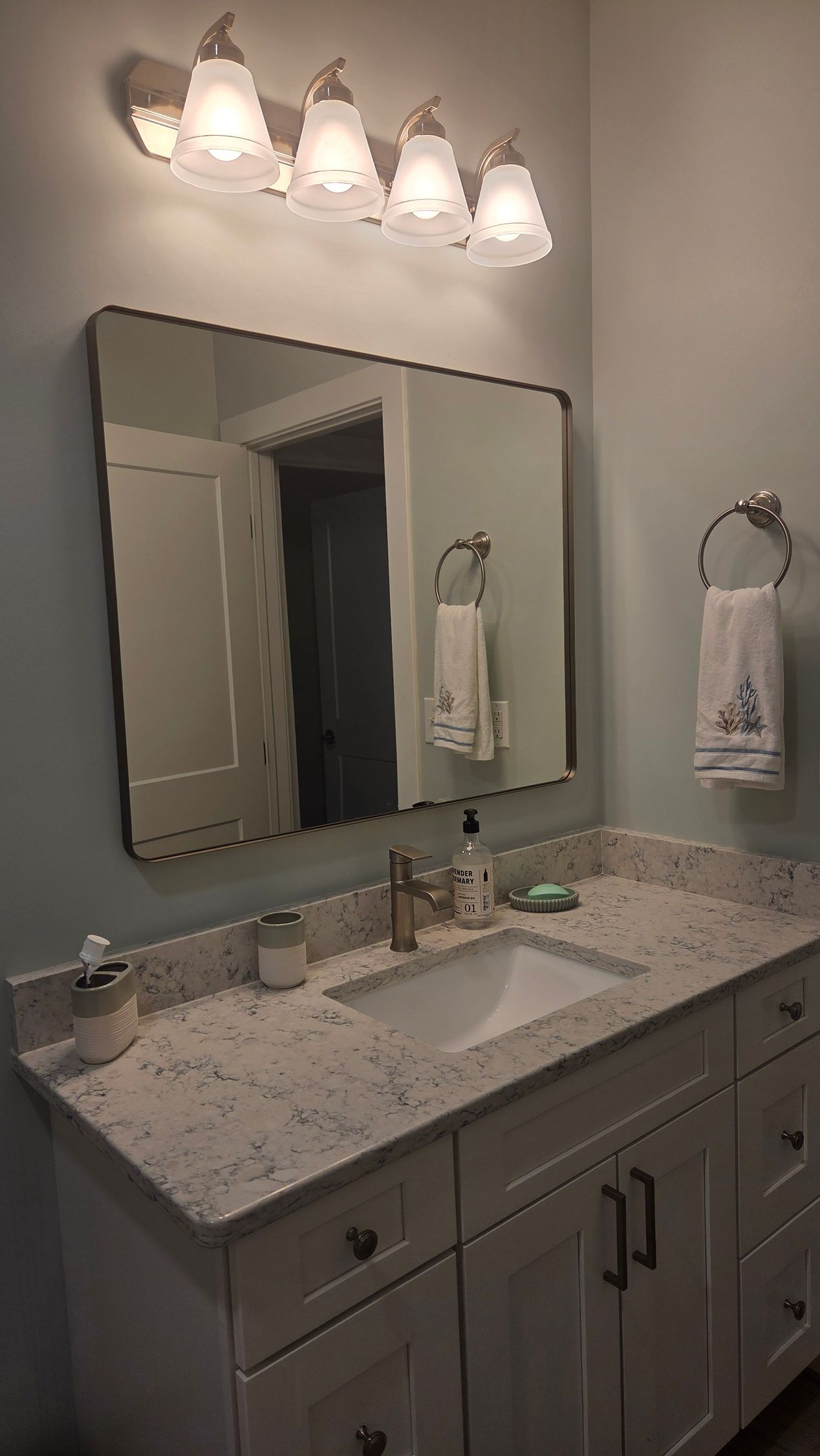 Bathroom vanity with granite countertop, mirror, and four light fixtures above a sink.