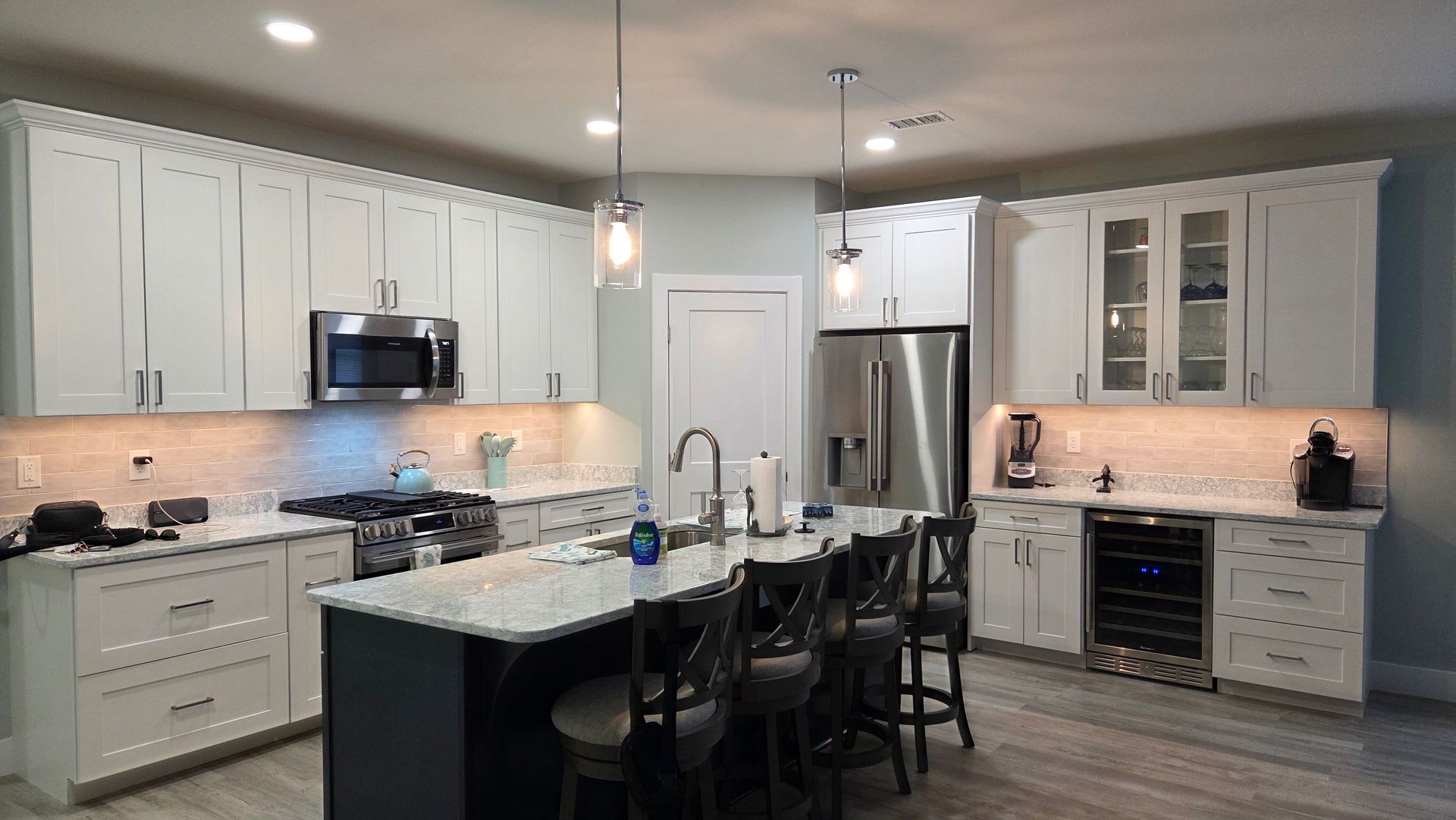 Modern kitchen with white cabinets, granite island, stainless steel appliances, and bar stools