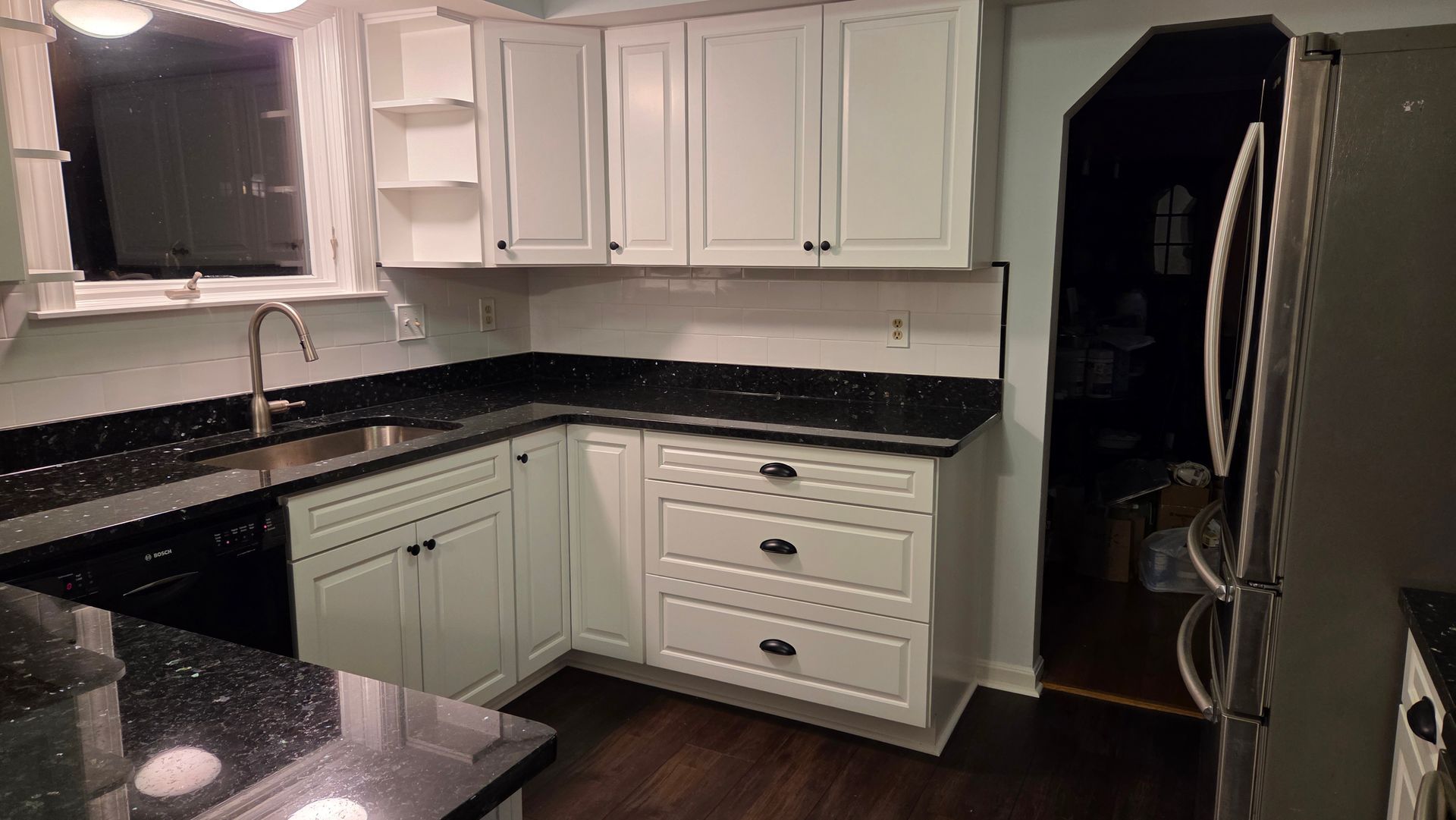 White kitchen cabinets with black countertops and a stainless steel refrigerator.