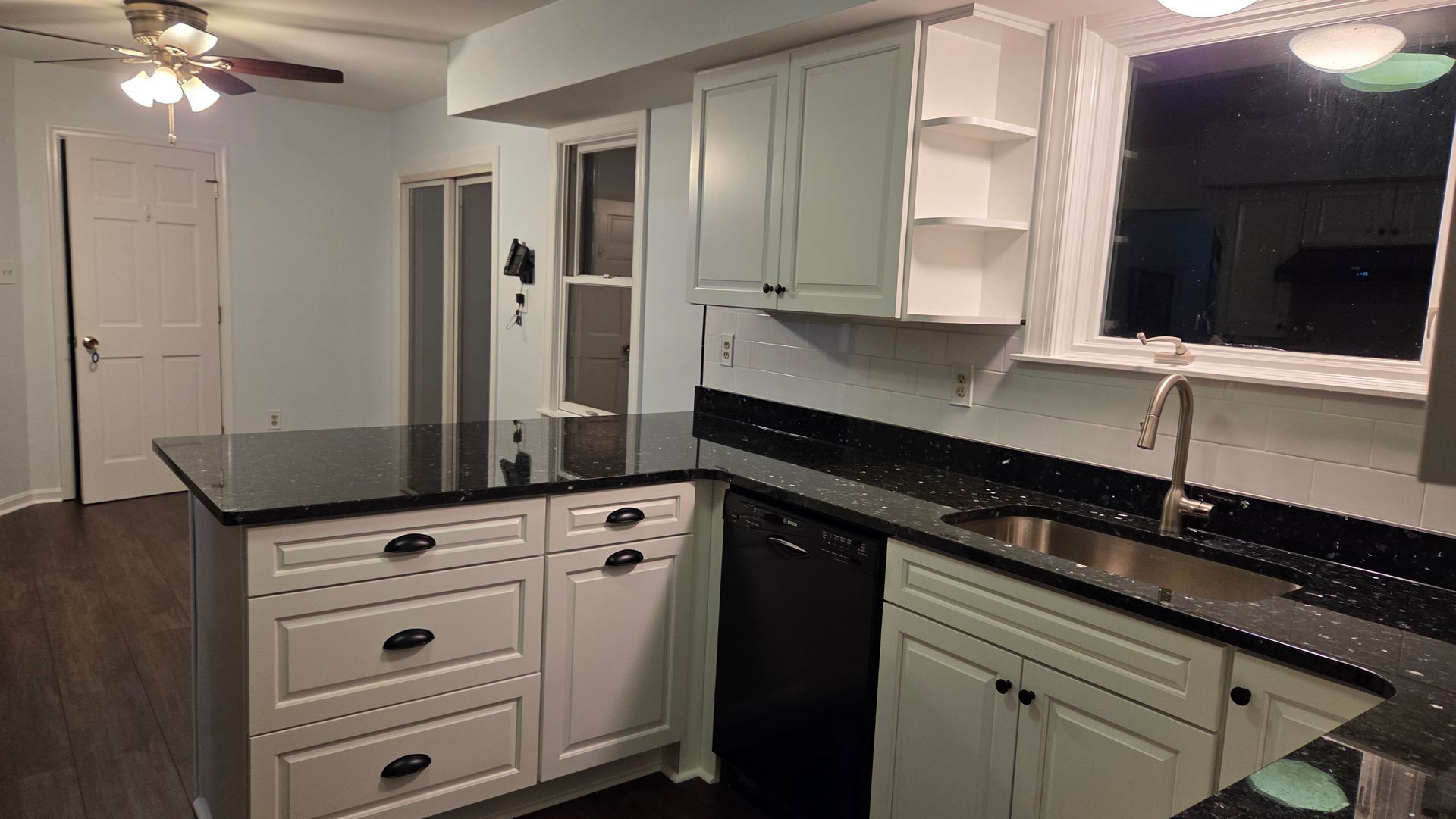 Kitchen with black countertops, white cabinets, and island; a dishwasher and sink are visible.