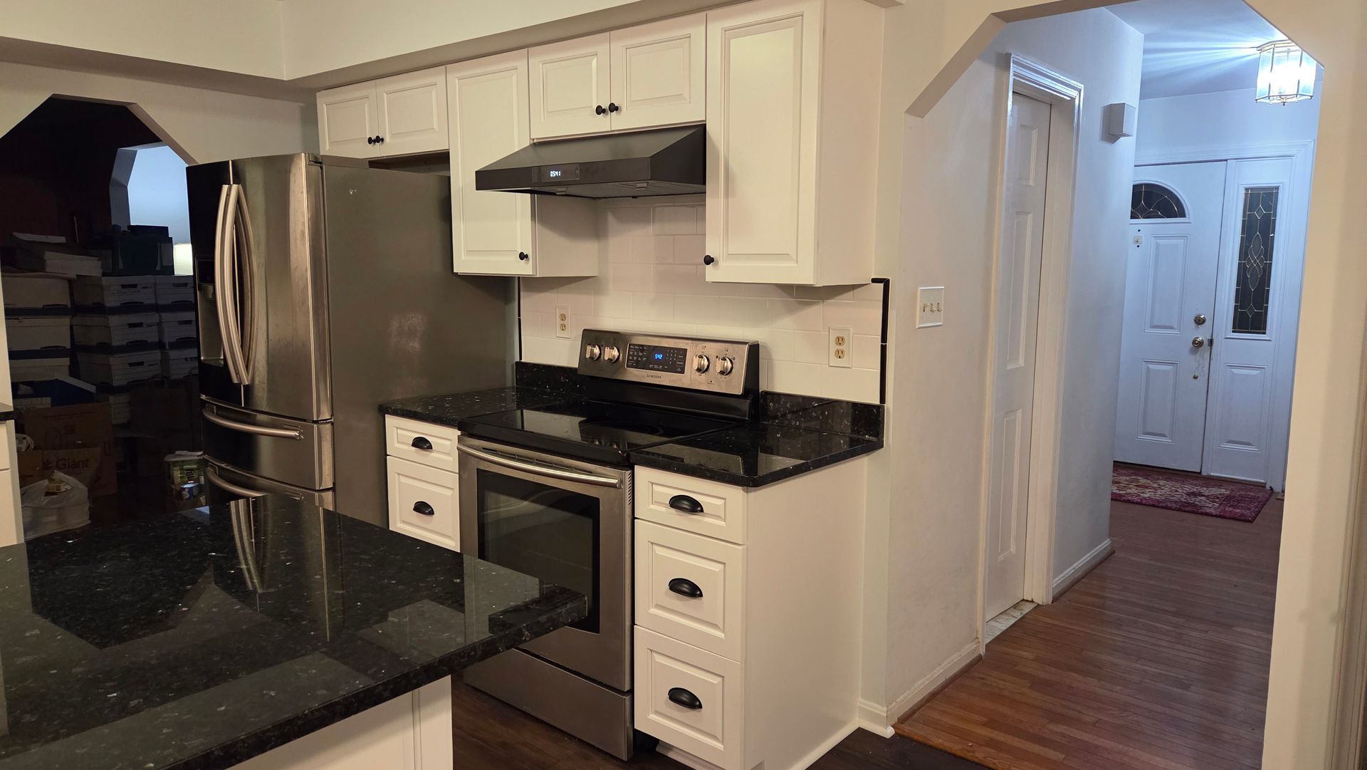 Kitchen with white cabinets, black countertops, stainless steel appliances, and a doorway to the right.