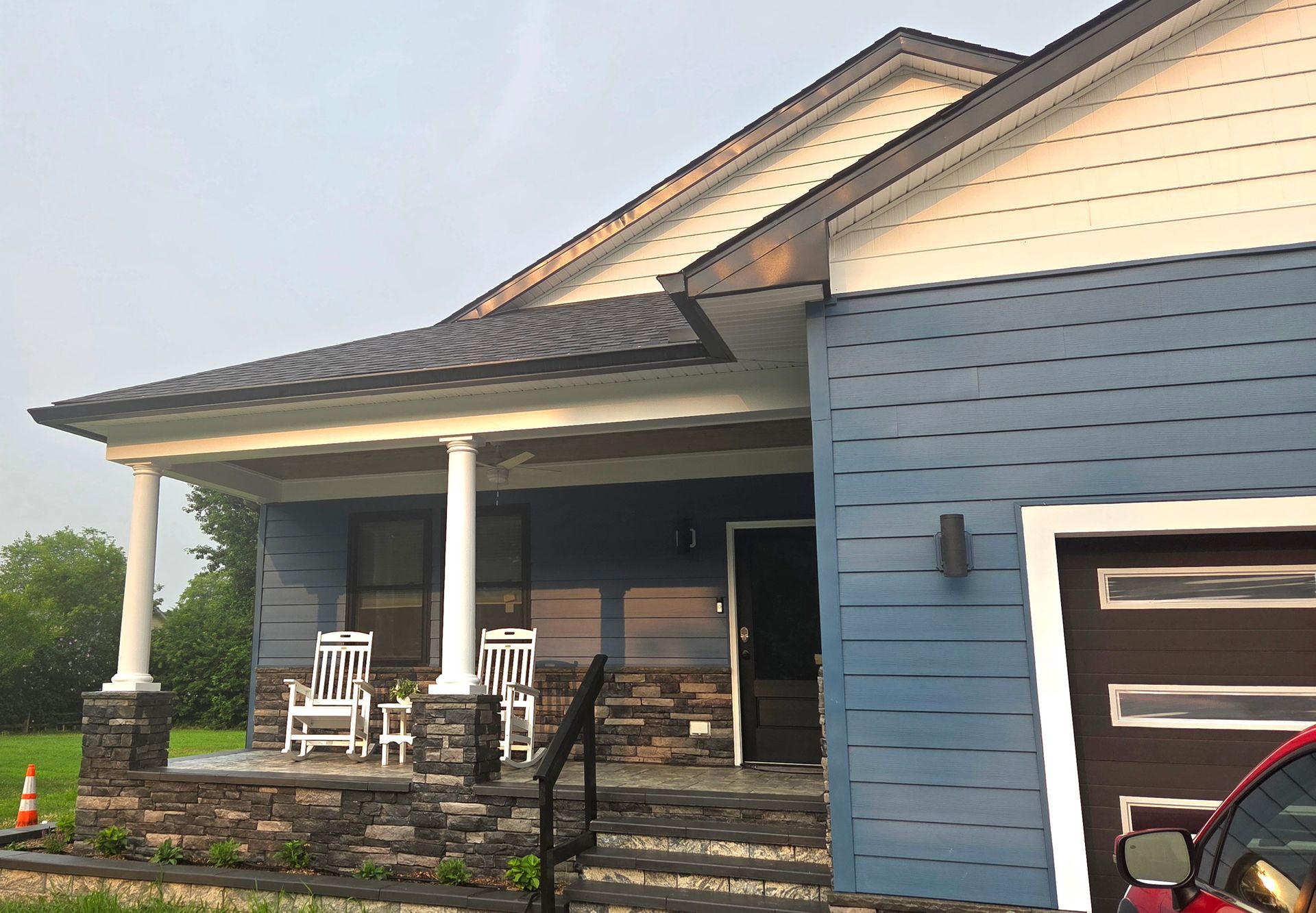 Blue house with white porch columns, two rocking chairs, and a dark garage door.