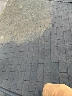 A person is standing on a brick sidewalk next to a roof.