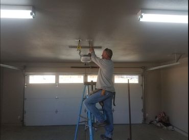 A man is standing on a ladder in a garage working on a garage door opener.