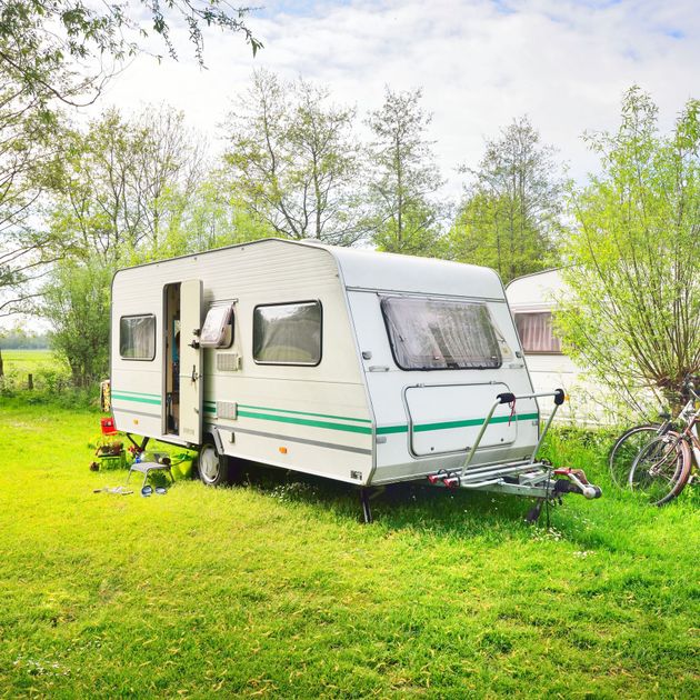 White camper trailer parked on a grassy campsite beside trees and a bicycle