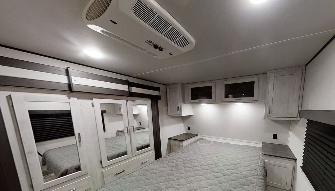 Modern white RV interior with bunk beds, cabinets, and ceiling vents