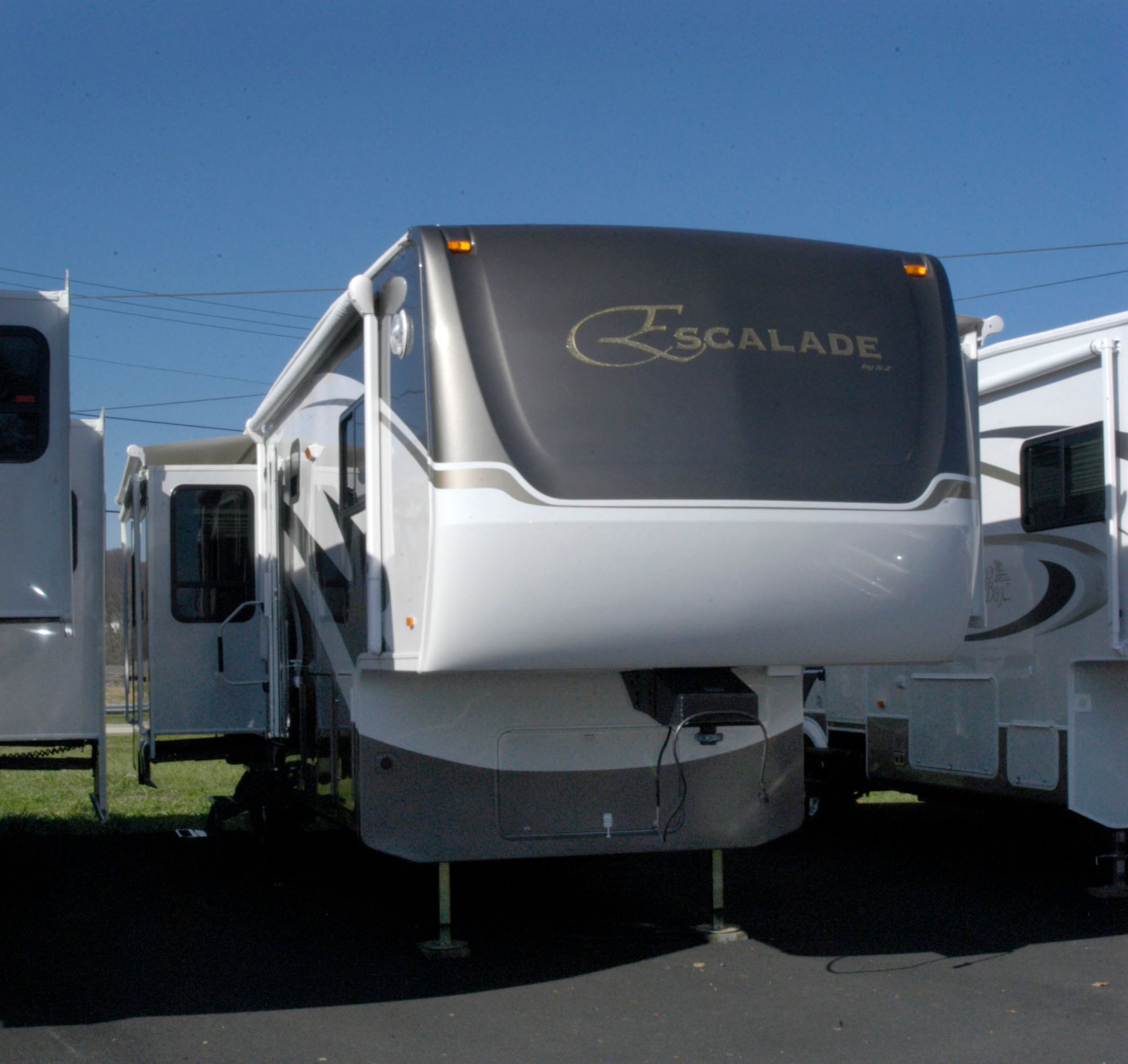 White and gray Escalade fifth-wheel RV trailer parked between other RVs on a lot
