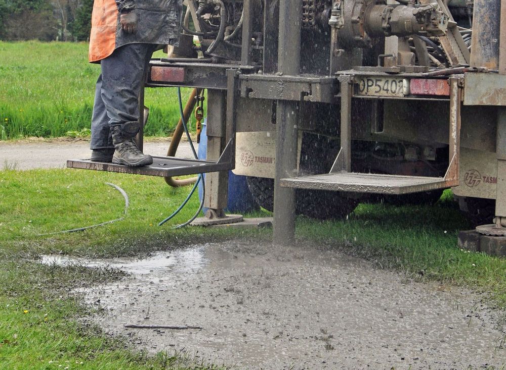 A man is standing next to a truck that is drilling a hole in the ground.