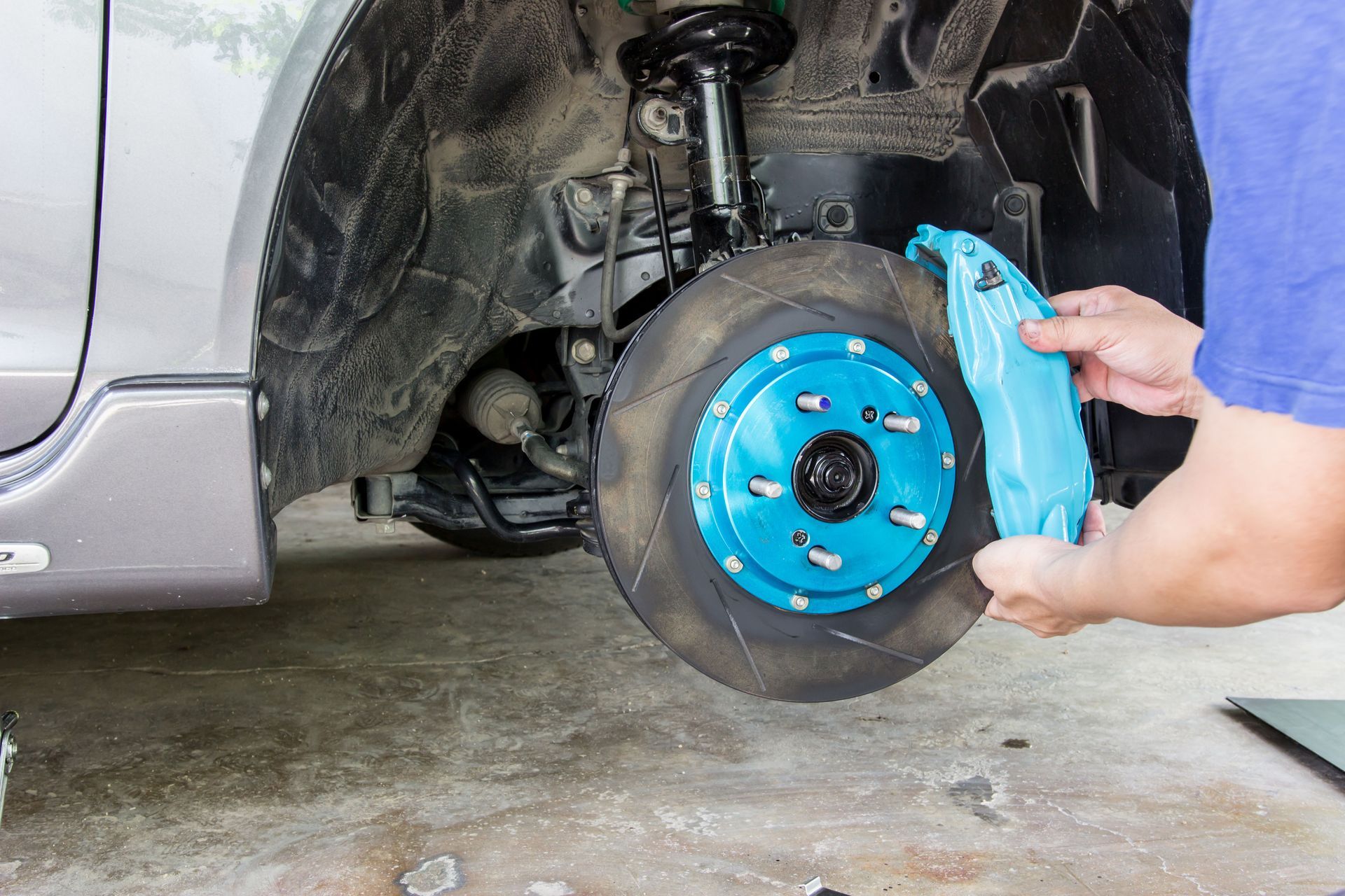 Hands installing a bright blue brake rotor on a car wheel hub in a garage.