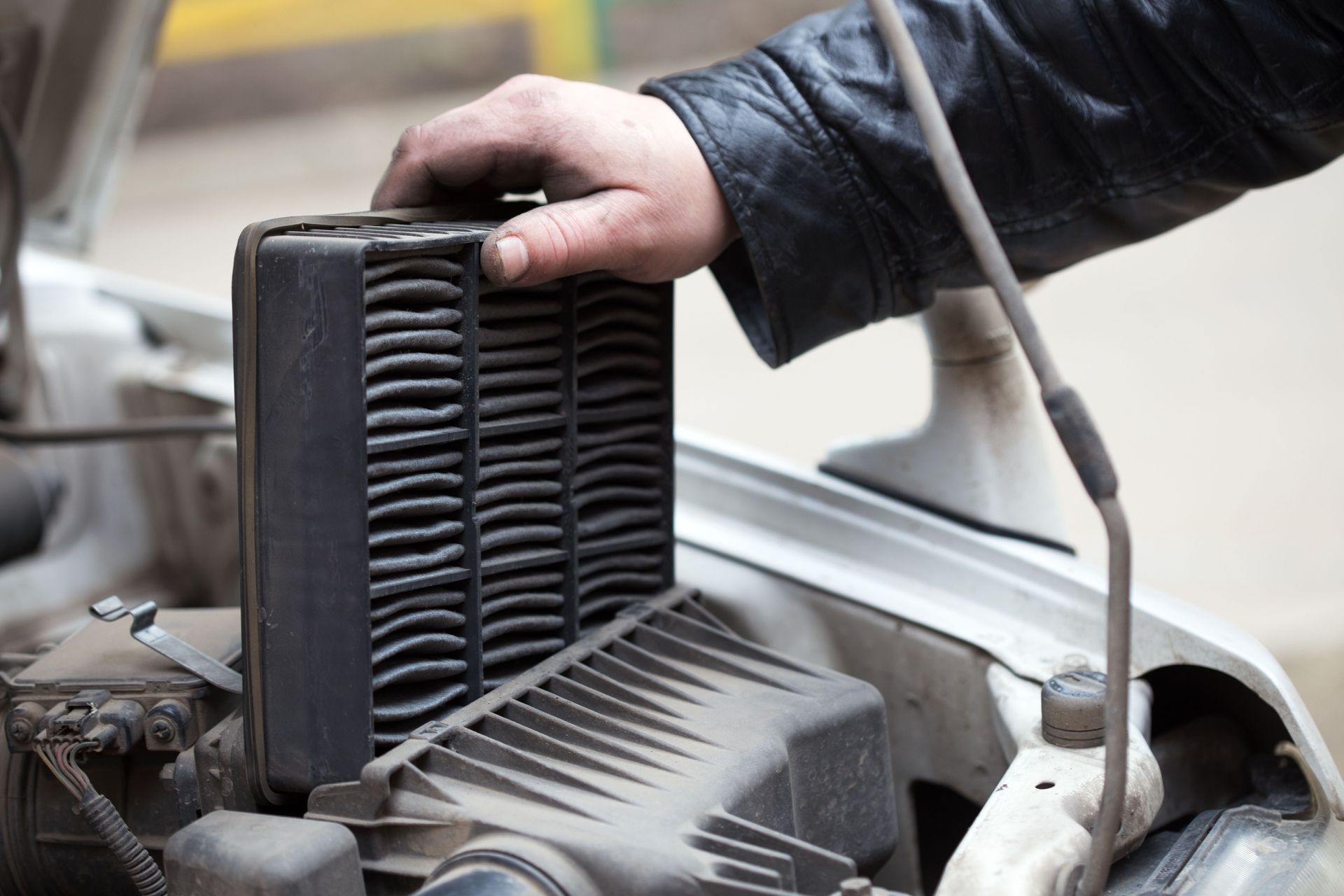 Hand holding a black car air filter above an open engine compartment